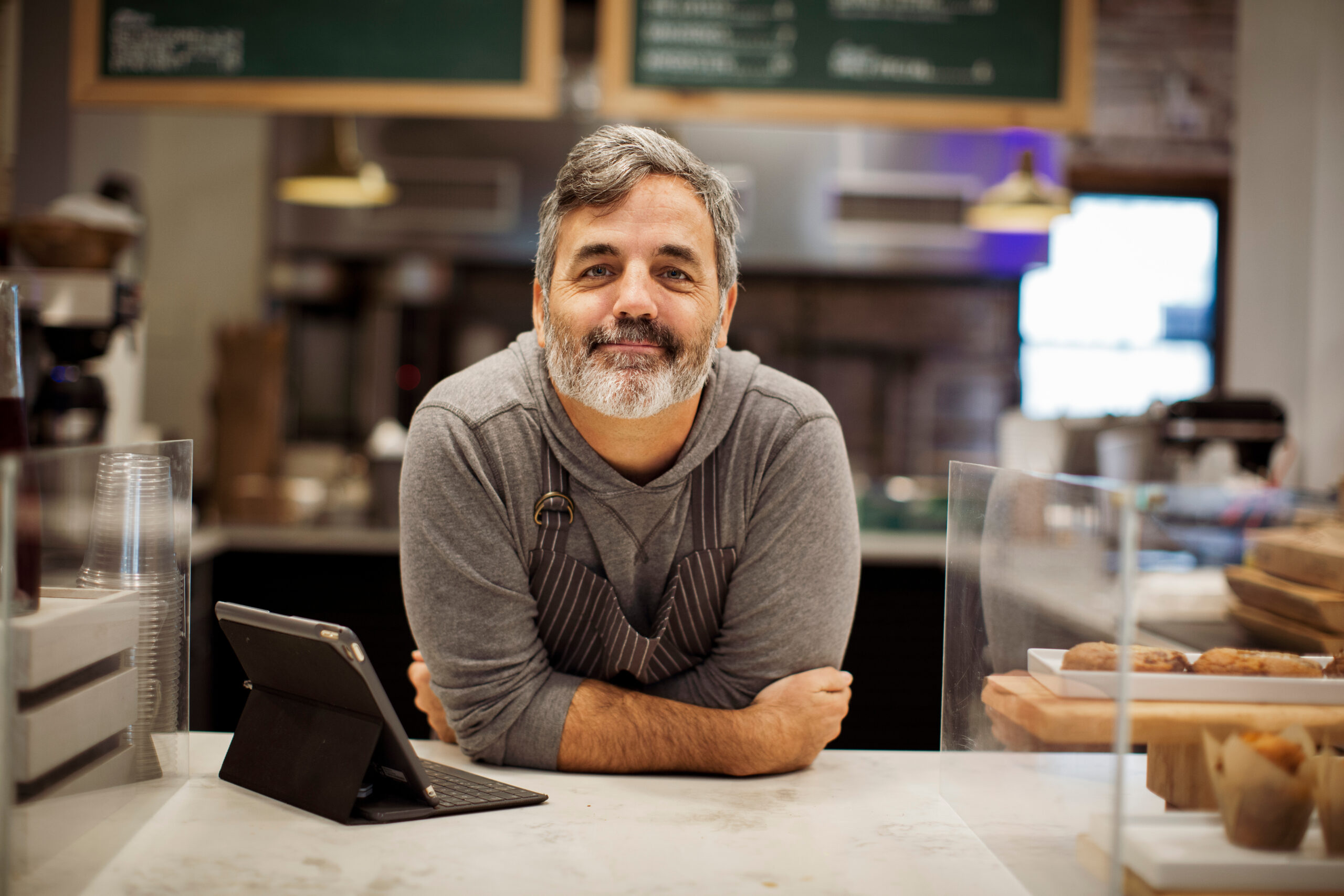 portrait of smiling male owner with tablet computer on bar counter